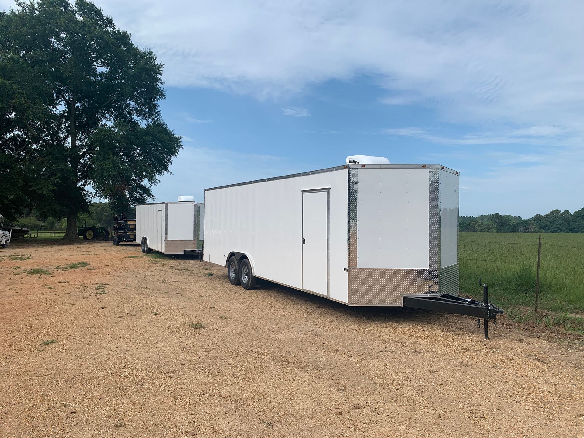 Two white trailers are parked next to each other in a gravel lot.