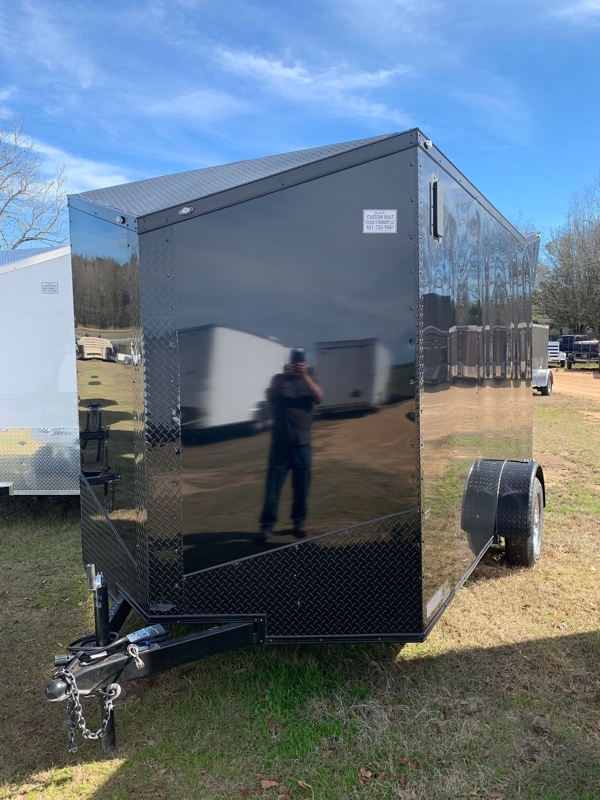A man is standing in front of a trailer in a field.