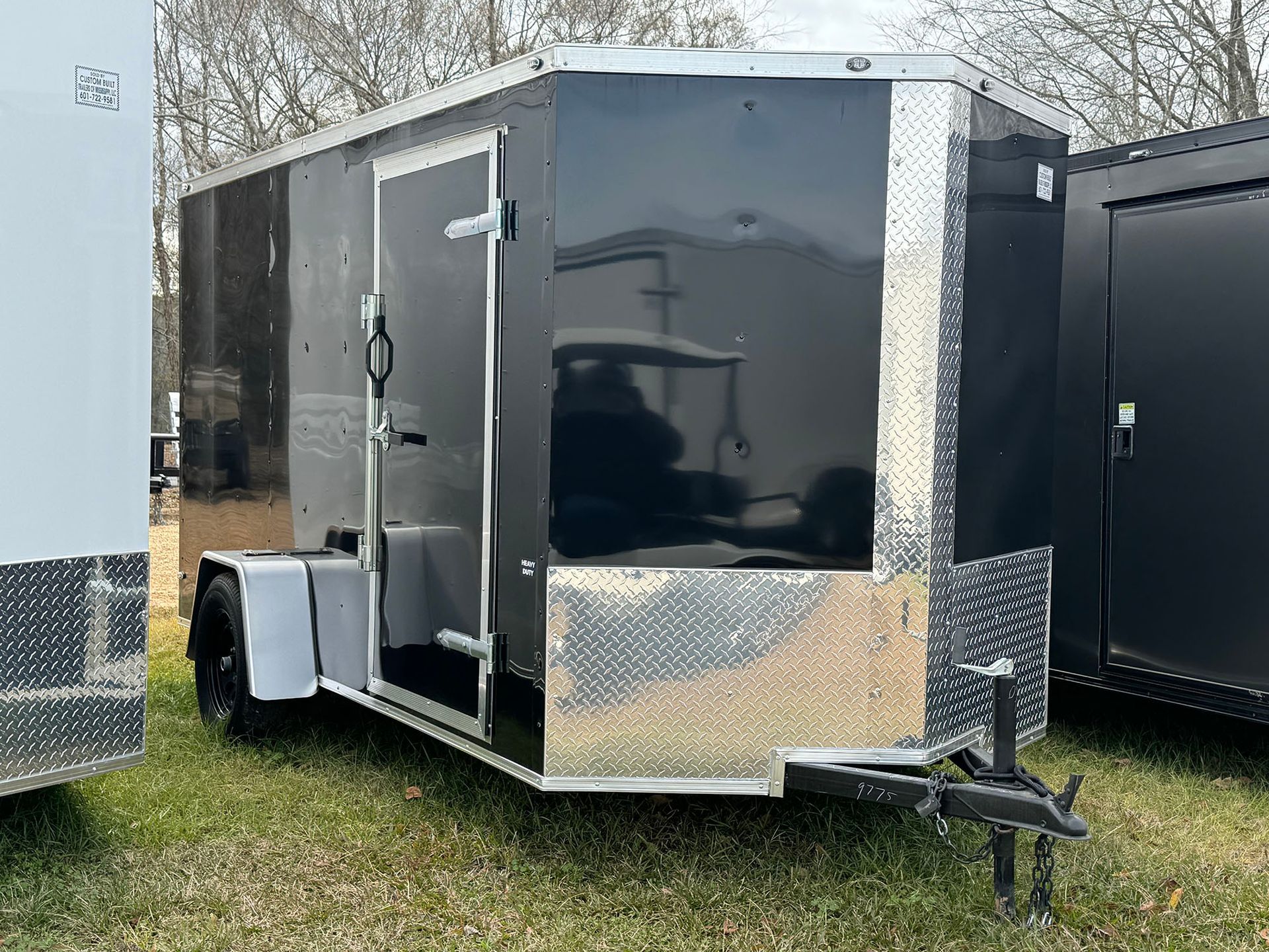 A black trailer is parked in the grass next to a white trailer.