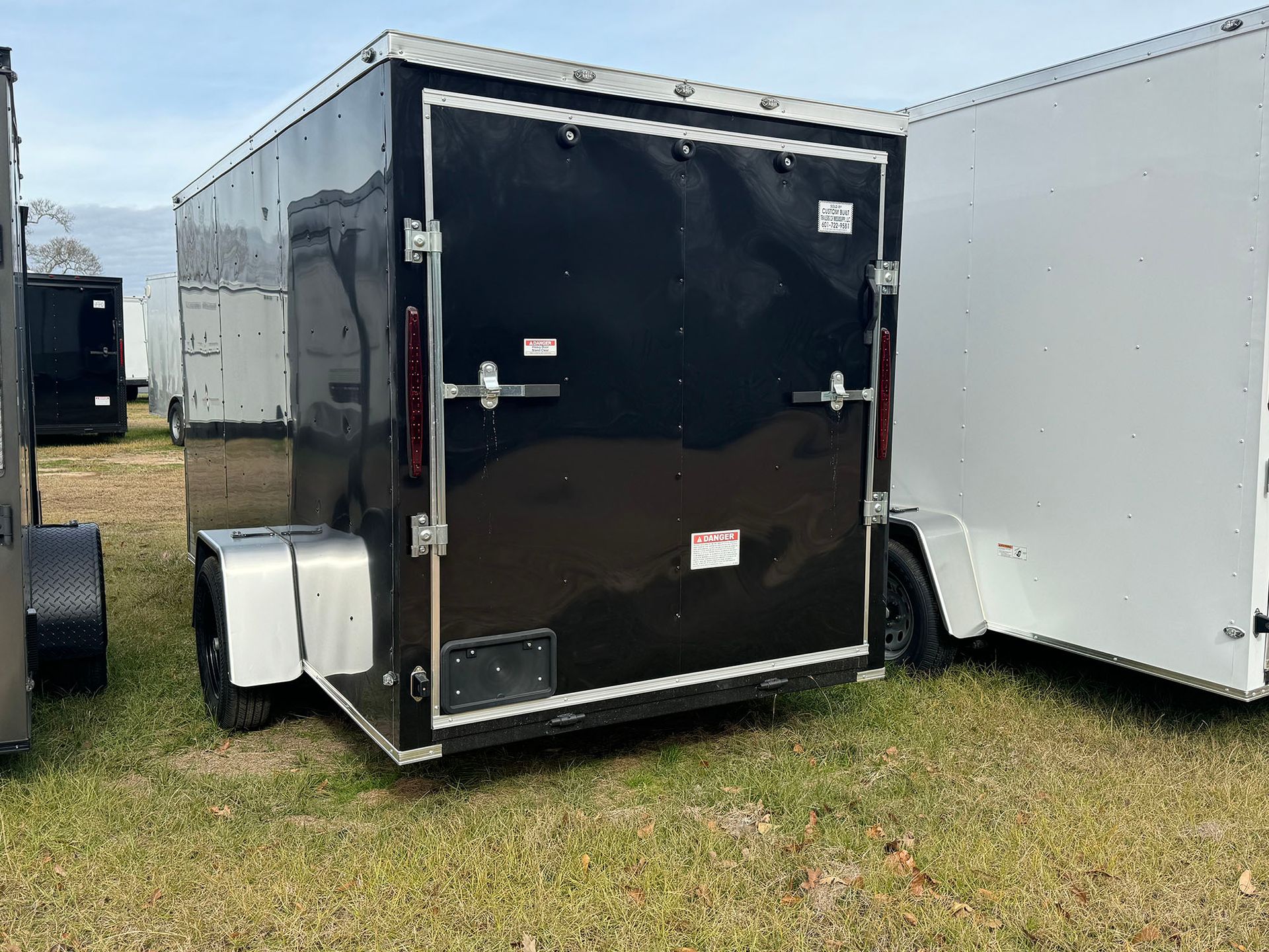 A black trailer is parked next to a white trailer in a grassy field.