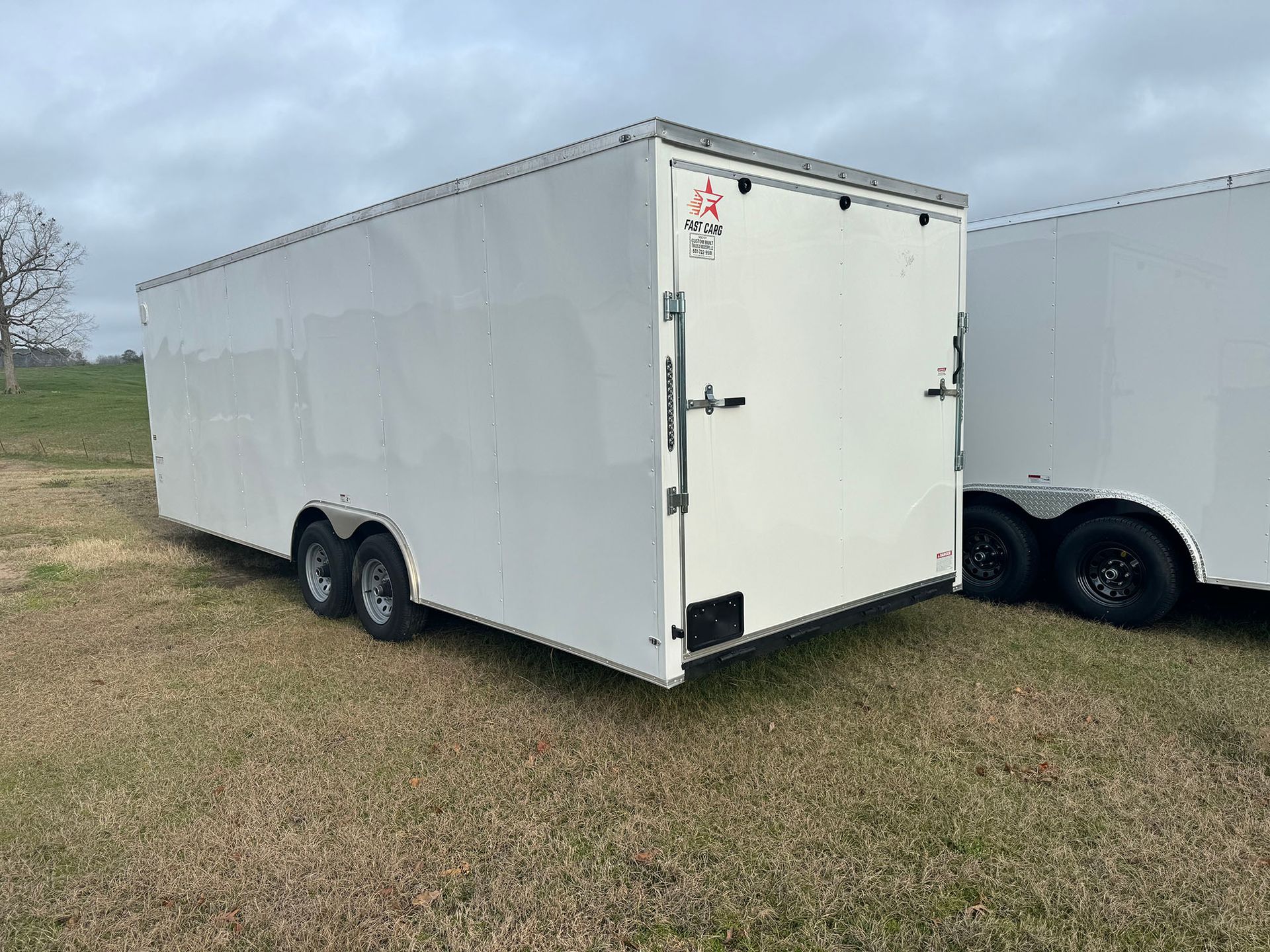 Two white trailers are parked in a grassy field.