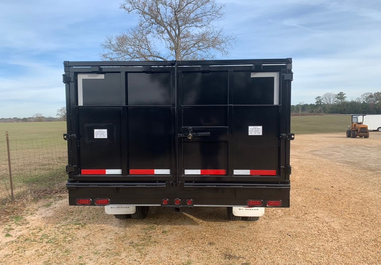 The back of a dumpster trailer is parked in a gravel lot.