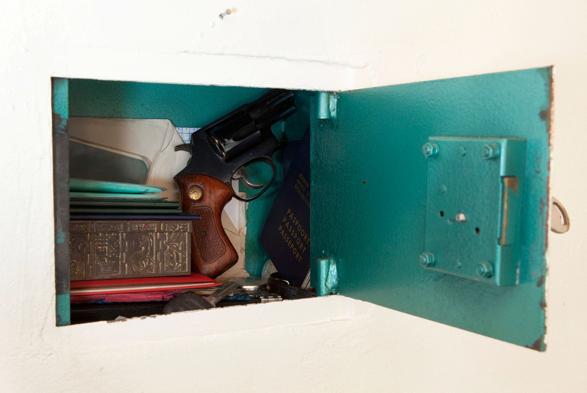 Open, turquoise wall safe reveals a gun, ties, and other items.