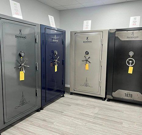Four large, metal gun safes in gray, blue, and black, in a store on a light wood floor.