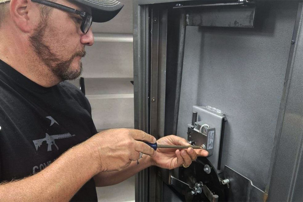 Man with a beard using a screwdriver on a safe's lock.