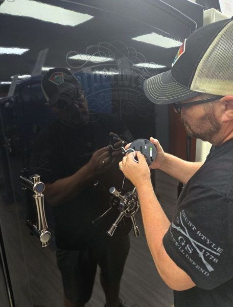 Man working on a black car door with a lock mechanism. Indoors with fluorescent lights.