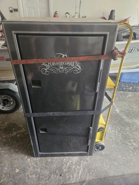 Black gun safe on a dolly, secured with a red strap, near a boat.