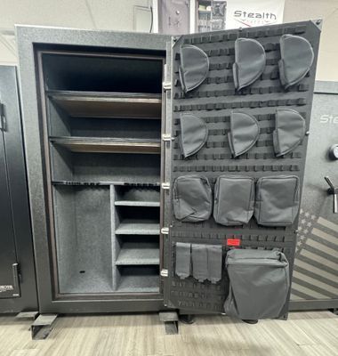 Open black gun safe, shelves on the left, organizer panel with pouches on the right, indoors.