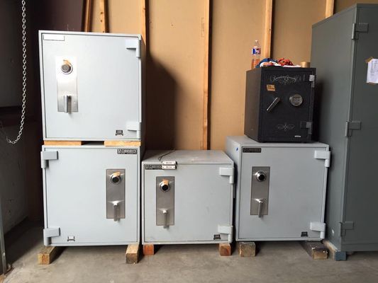 Row of large, gray safes of varying sizes with a small black safe on top. Wooden support blocks below the safes.