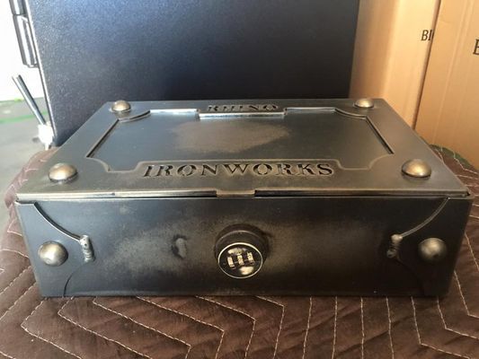 Black metal Ironworks strongbox with a lock, sitting on a quilted surface.