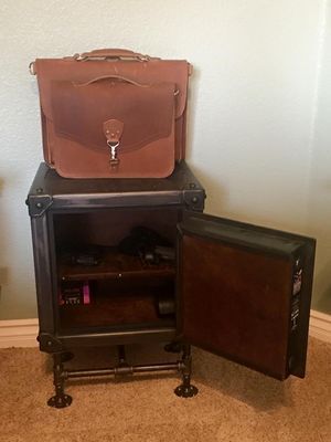 Brown leather briefcase on a dark metal cabinet, door open revealing contents.
