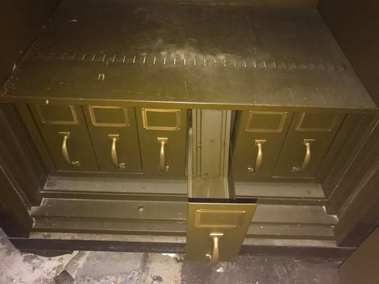 Inside of an old olive green metal cabinet with drawers and a drop-down door.