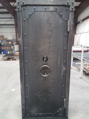 Large, dark metal safe with bolted details, circular handle, and vintage-style design, inside a workshop.