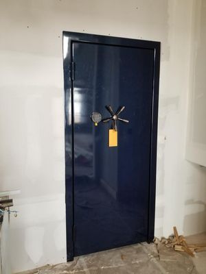 Blue safe door with dial and handle, installed in a room with white walls and debris.