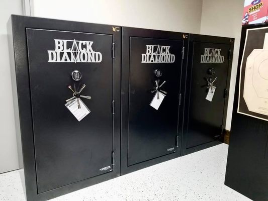 Three black Black Diamond gun safes lined up; a target in the background.