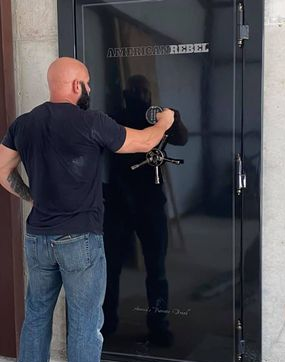 Man in jeans and black shirt opening a black safe door with