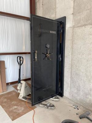 Black vault door ajar, with gold hardware, against a concrete wall. Pallet jack nearby.