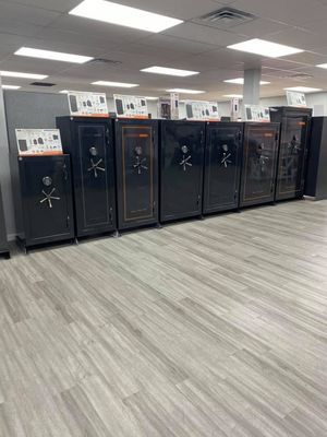 Row of black gun safes in a brightly lit store with wood-look flooring.