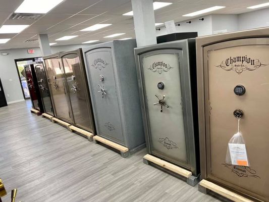 A row of gun safes in a store. Gray, tan, and brown safes on wooden supports.