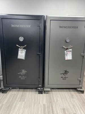 Two Winchester gun safes, one black and one gray, standing side by side in a store.