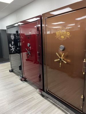 Row of colored safes: black, red, and brown with gold hardware and logo in a store.