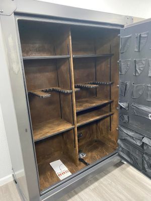 Open gray gun safe with wood-lined interior, shelves, and gun racks.