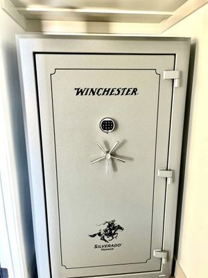 Silver Winchester gun safe, light gray, with combination lock and large handle, inside a room.