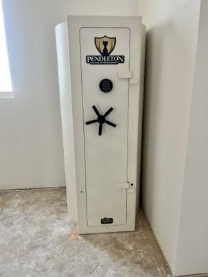 A cream-colored Pendleton gun safe stands in a corner of a room with unfinished walls and flooring.