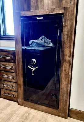 A black gun safe with a combination lock, built into wooden cabinetry.  Inside is a shelf with a blue cloth.