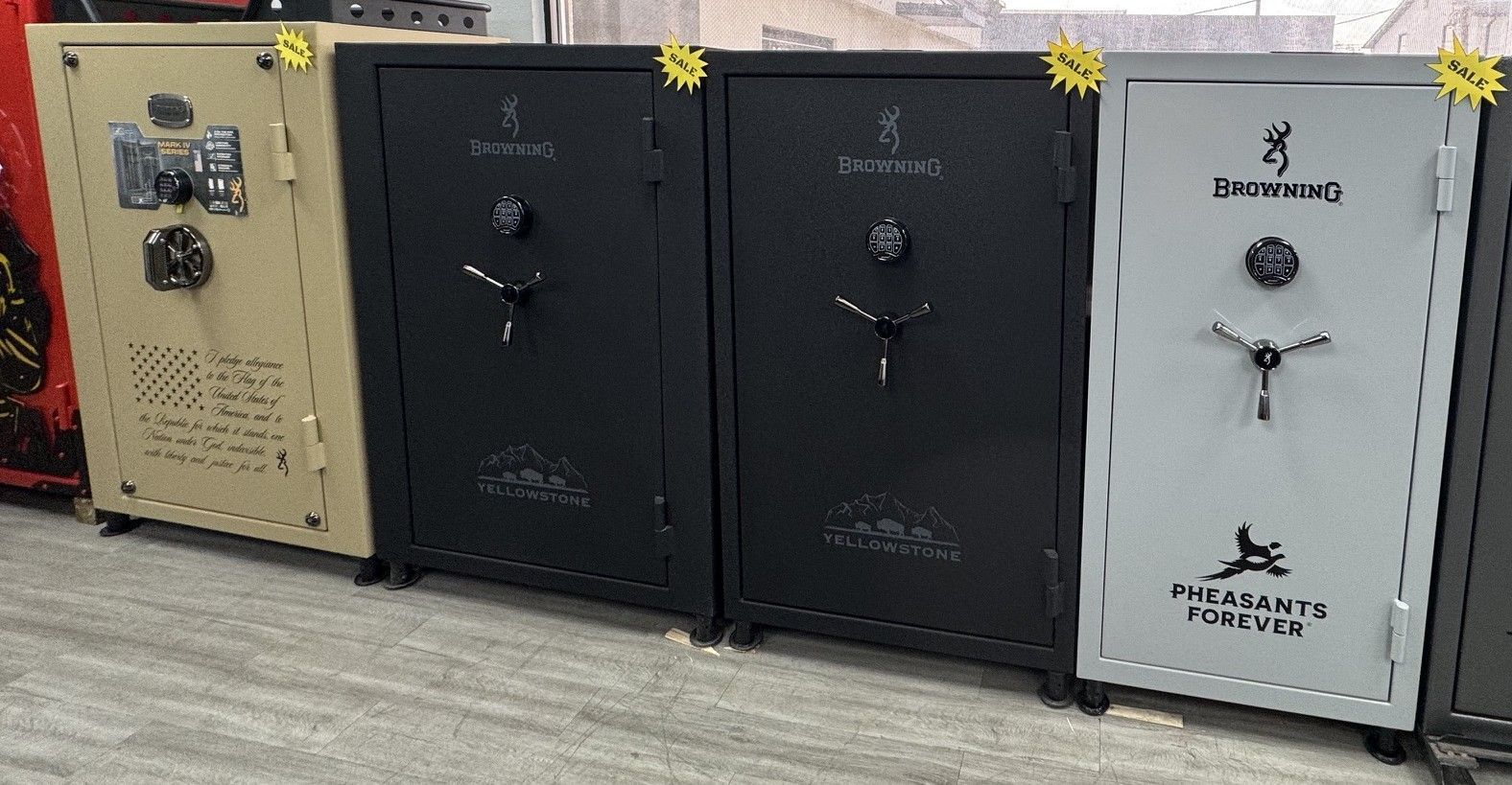 Three large gun safes in beige, black, and white lined up indoors on a floor.