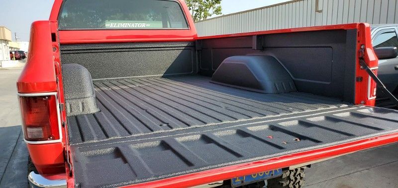 A red truck with a black bed is parked in front of a building.