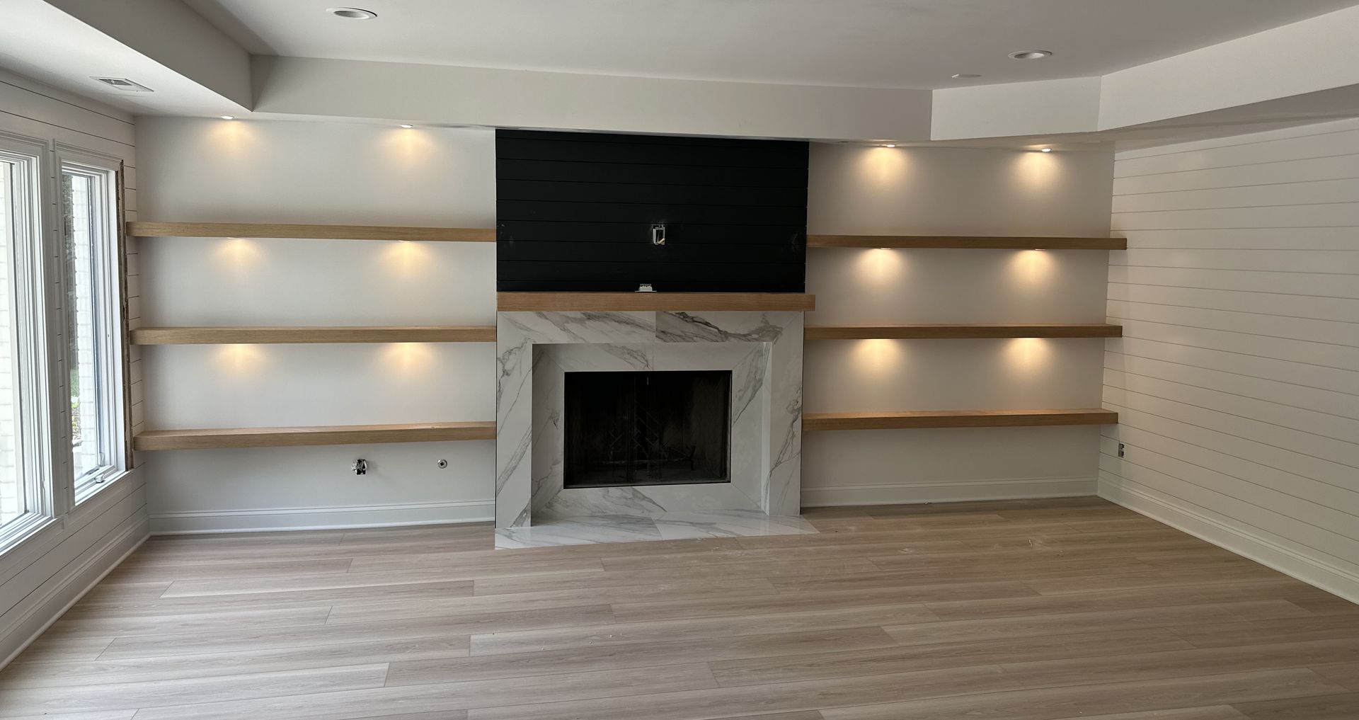 Empty living room with a white built-in fireplace, dark TV niche, and wall shelves with recessed lighting