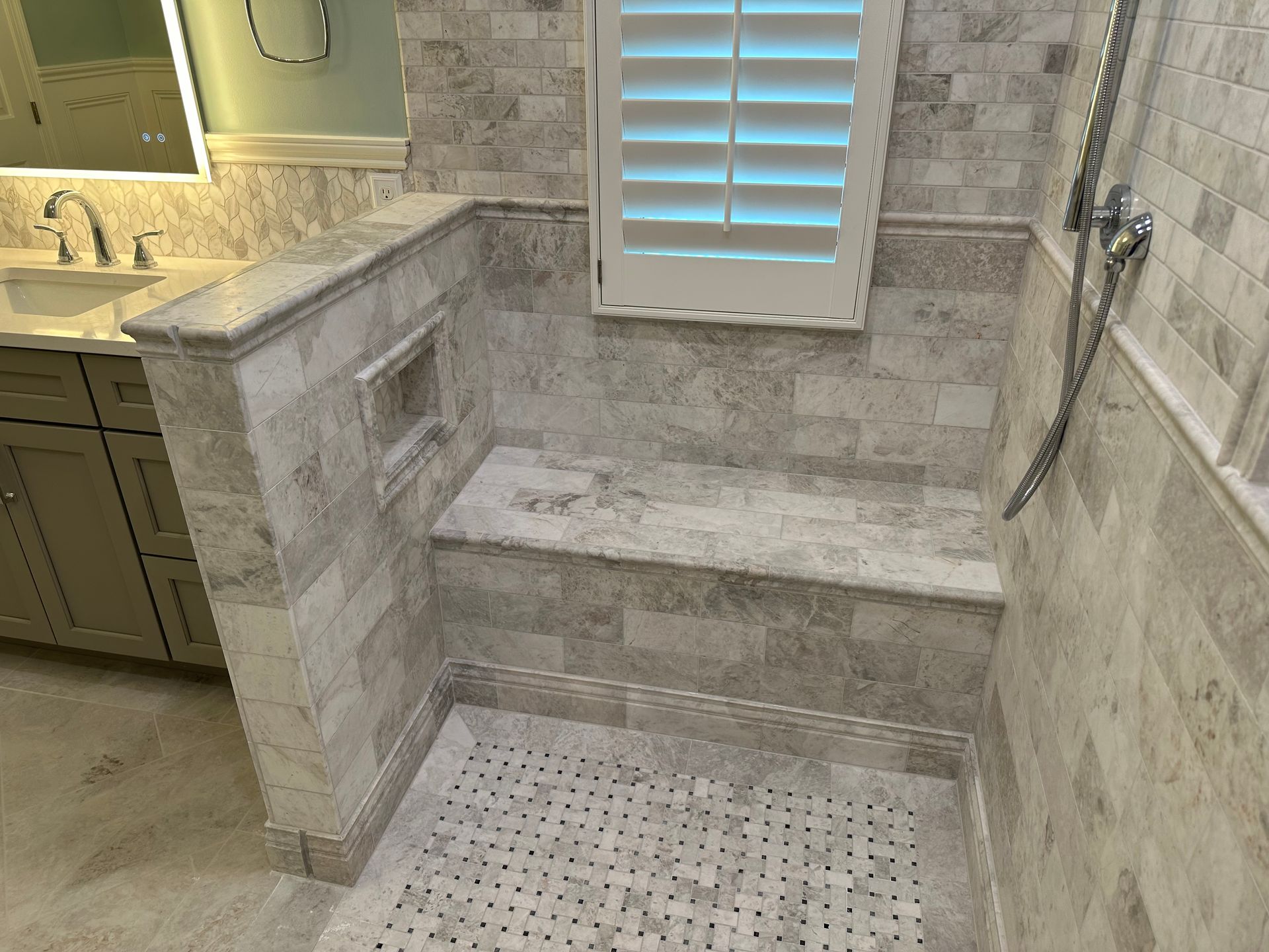 Stone-tiled bathroom with a built-in shower bench, window shutters, and a sink vanity on the left.