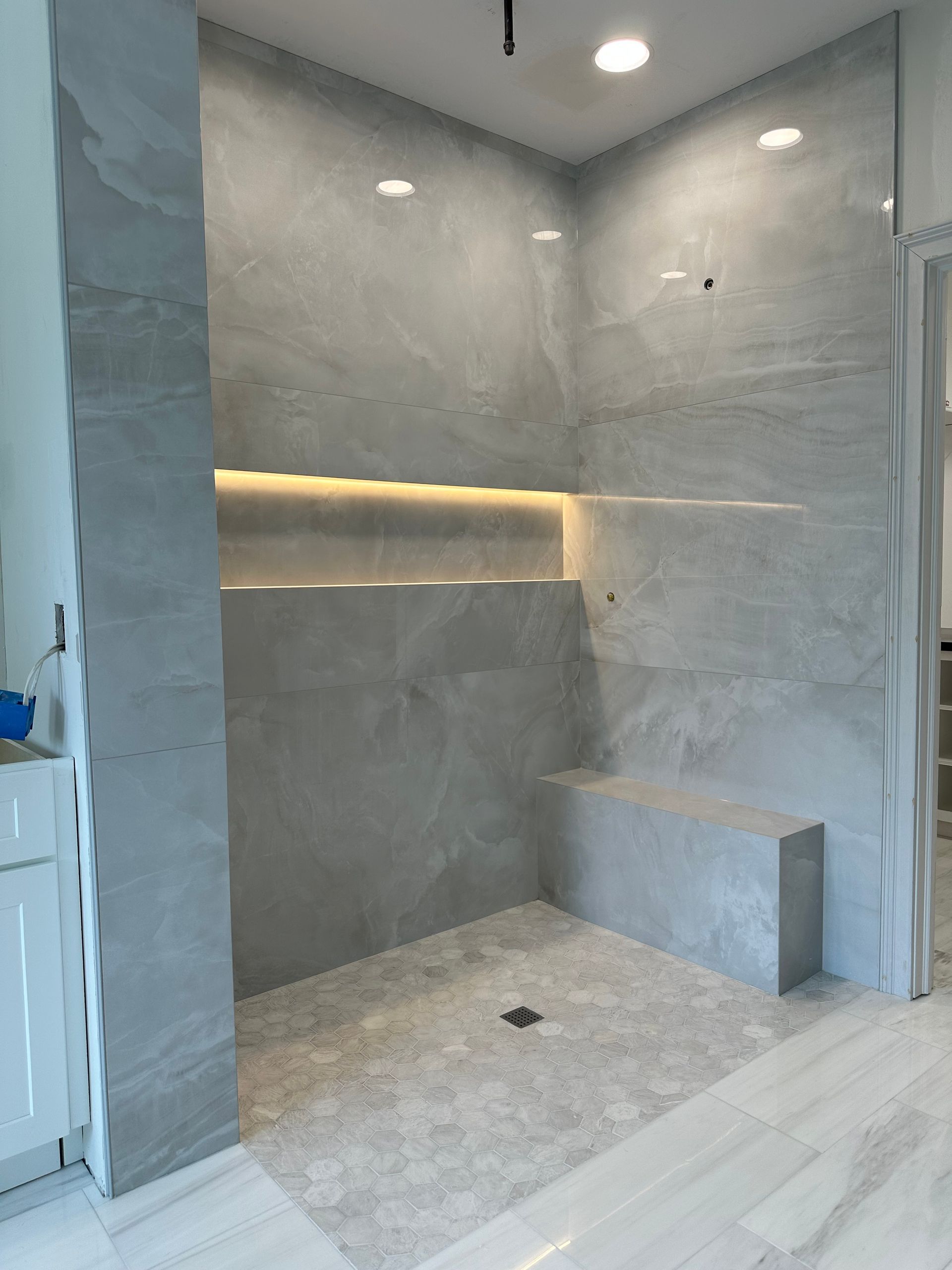Modern tiled walk-in shower with built-in bench and warm recessed lighting