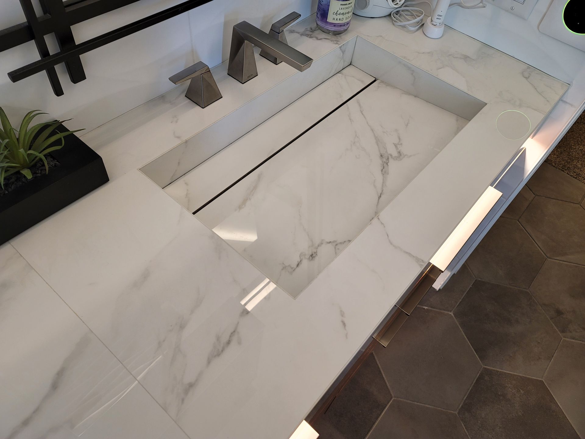 Modern white marble kitchen counter with built-in sink and dark hexagon floor tiles.