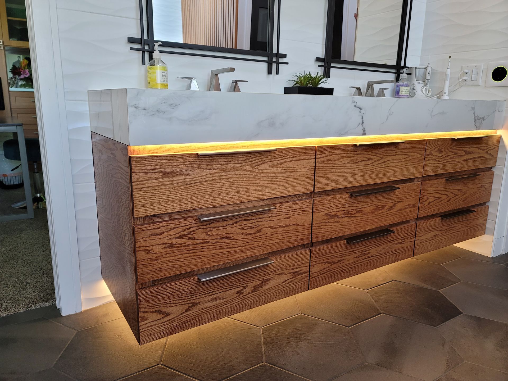 Modern outdoor vanity with wood drawers, white countertop, and warm under-cabinet lighting under windows