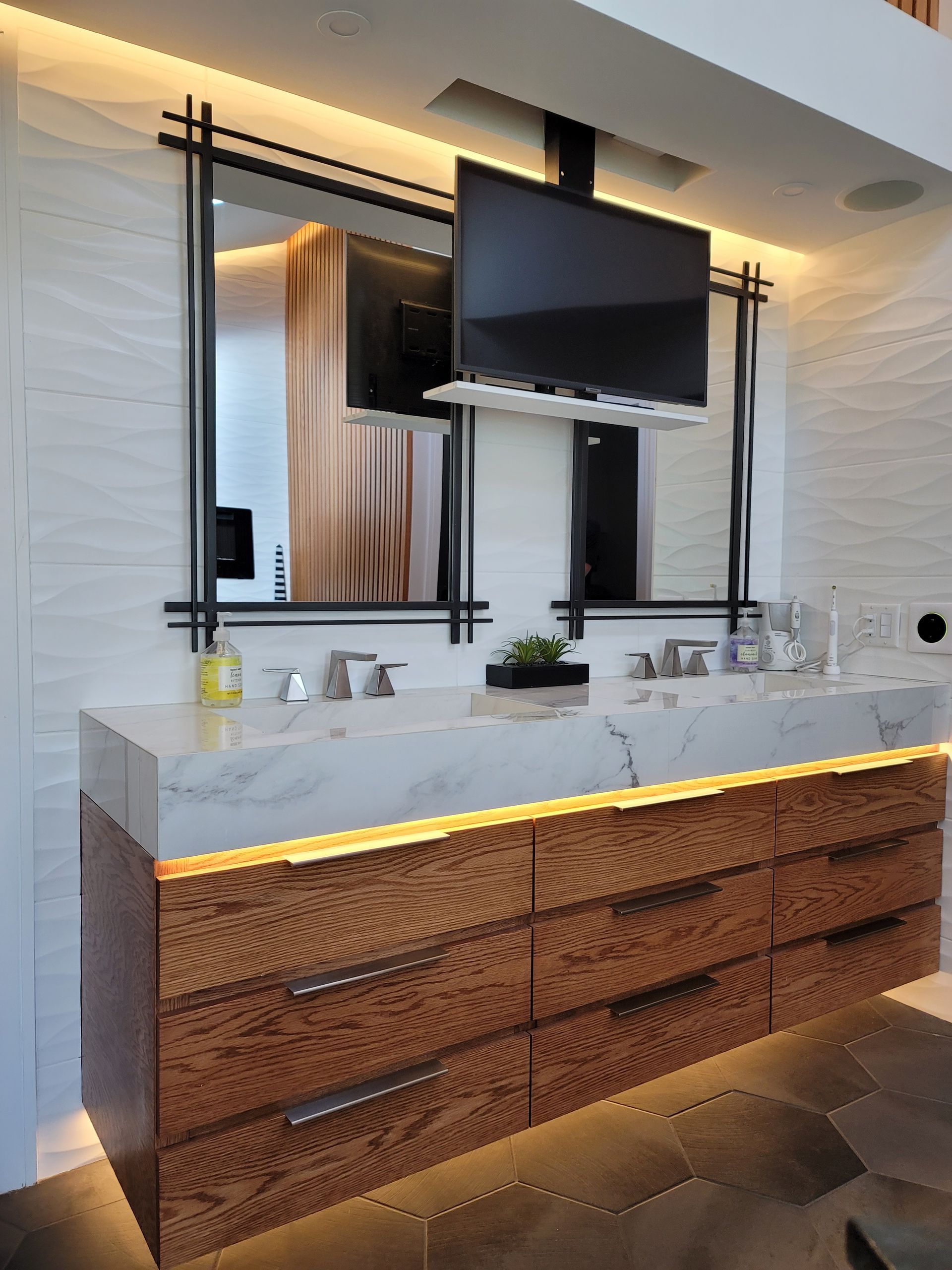Modern bathroom vanity with marble countertop, wood drawers, lit mirror, and wall-mounted TV
