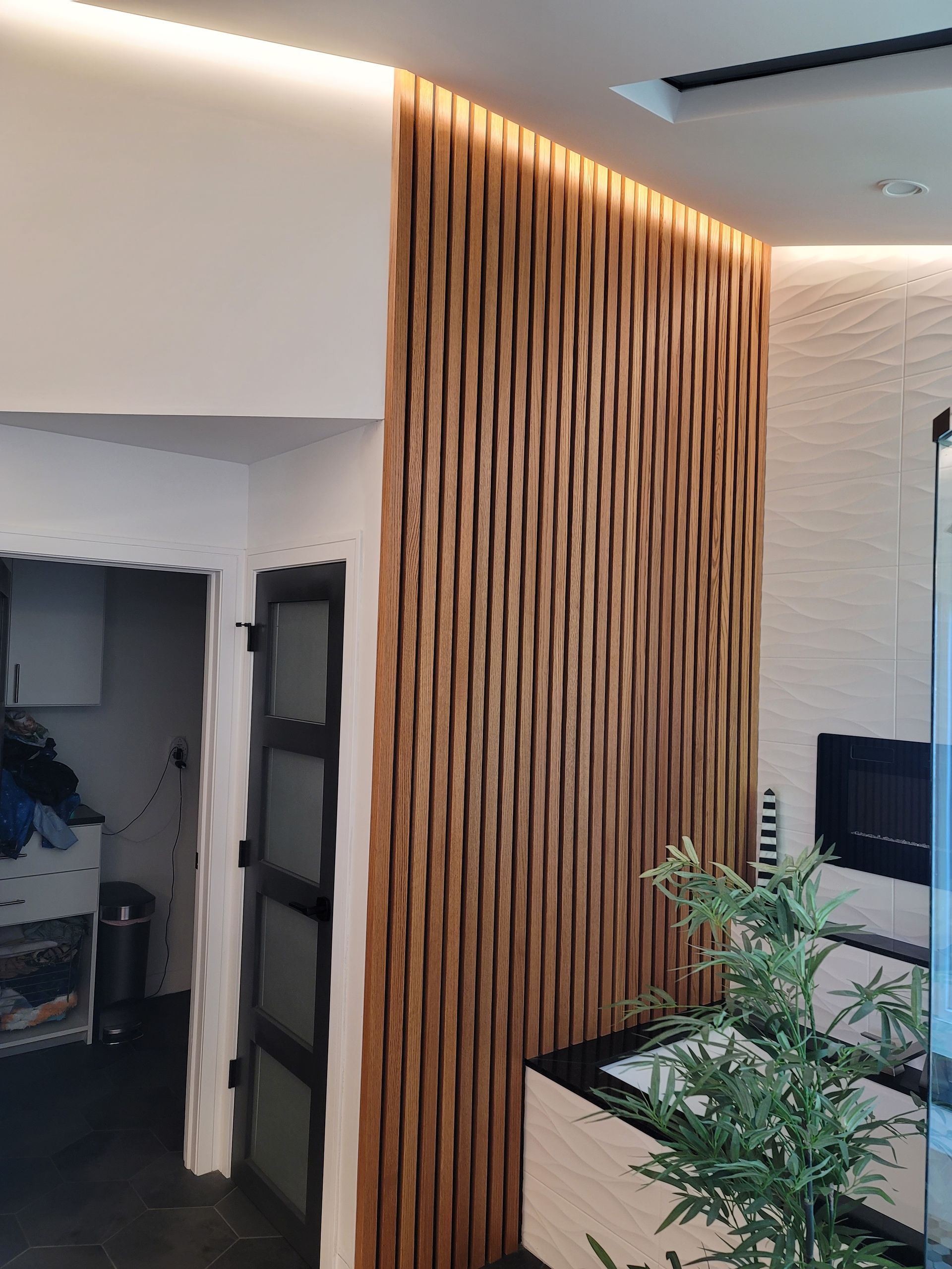 Modern interior with wood slat wall, recessed ceiling lights, and a plant beside a counter.