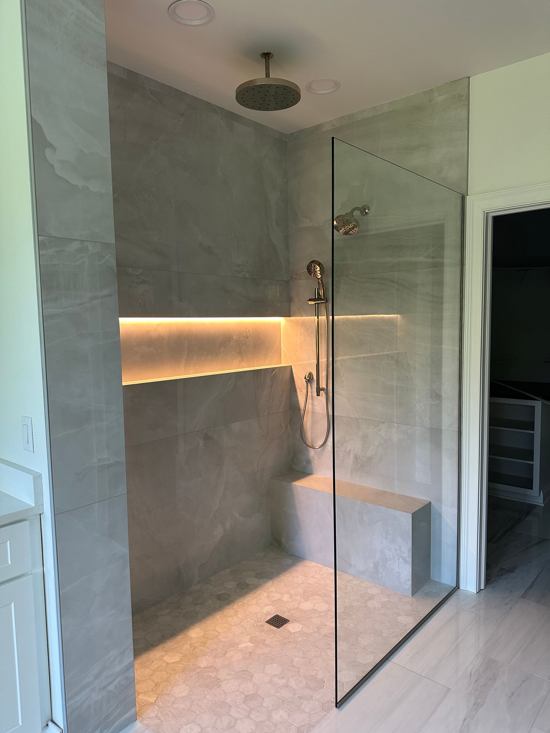 Modern bathroom with a glass shower enclosure, gray tile walls, and warm backlit niche.
