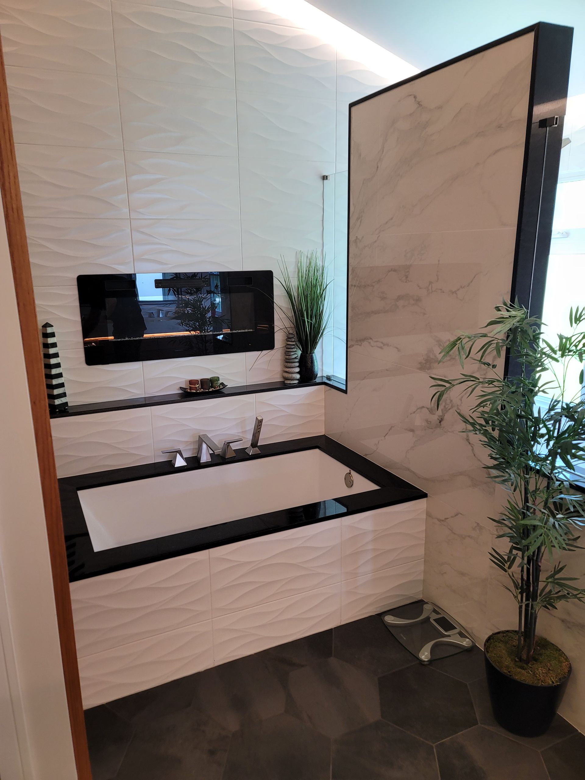 Modern bathroom with a black-and-white vanity, mirror, open shower partition, and potted plant