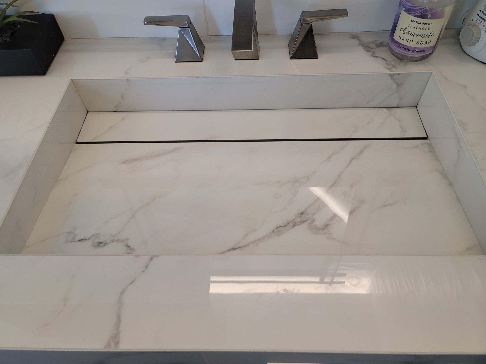 White marble bathroom sink with two faucets and a soap dispenser on the counter