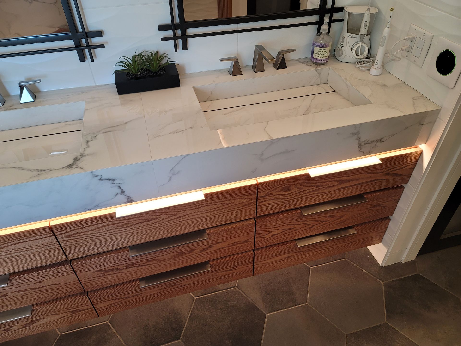 Modern bathroom vanity with white countertop, copper drawer fronts, hex tile floor, and black fixtures
