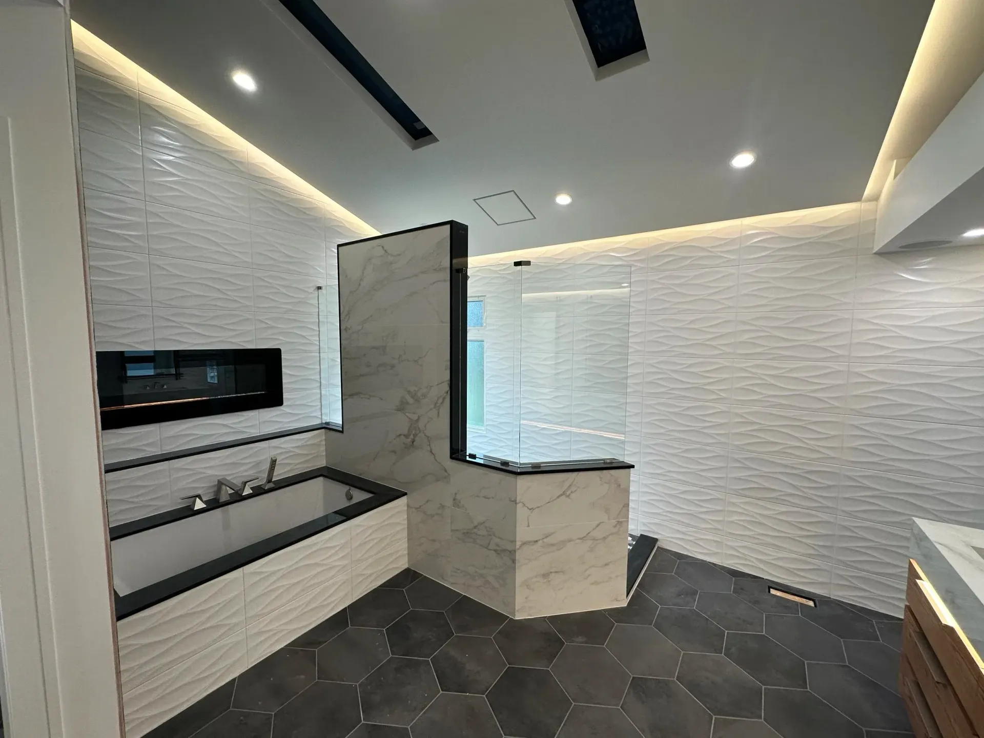 Modern bathroom with white textured walls, dark tile floor, and a walk-in shower area with glass partition.