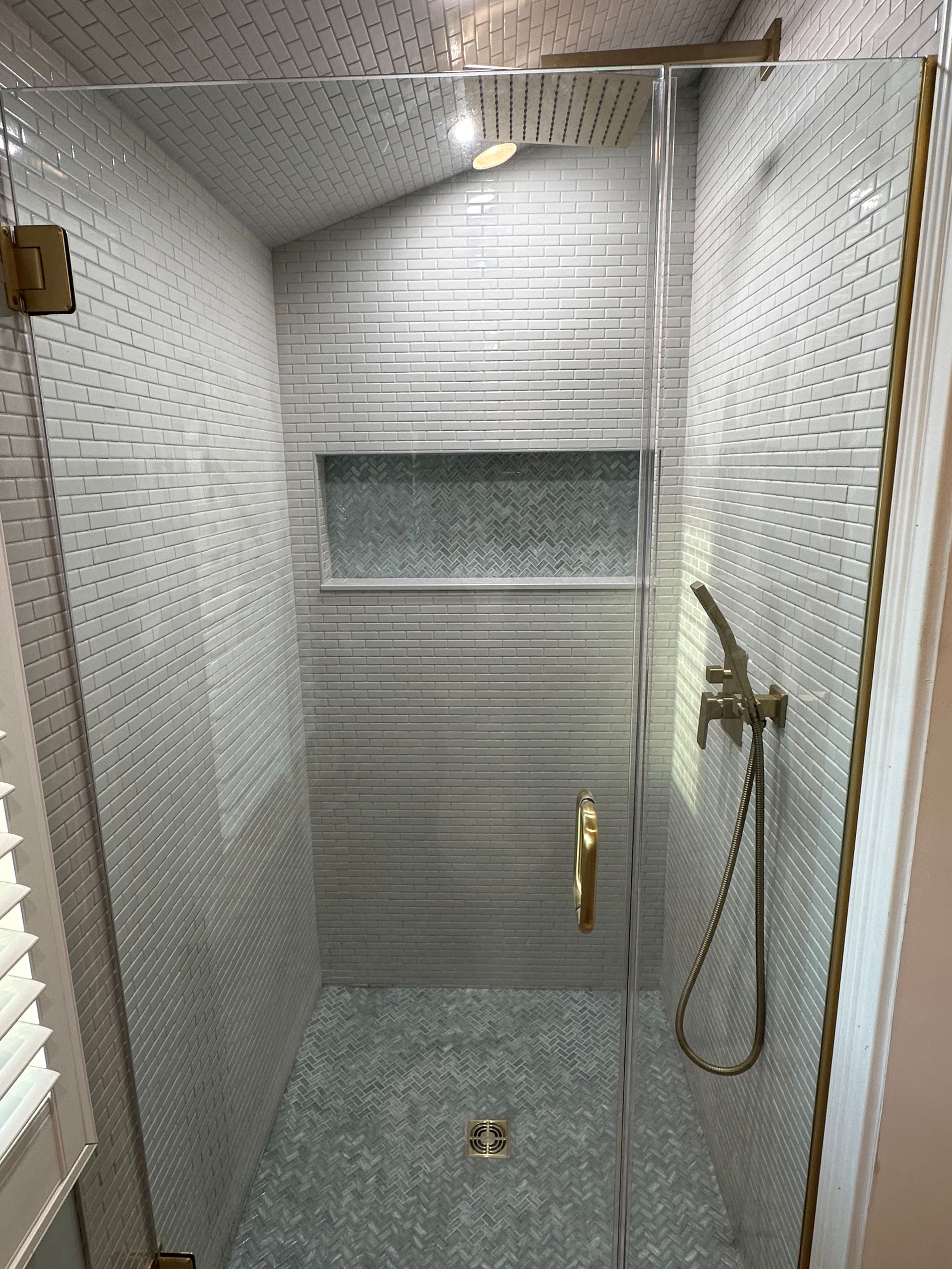 Small tiled shower stall with glass door, showerhead, and floor drain.