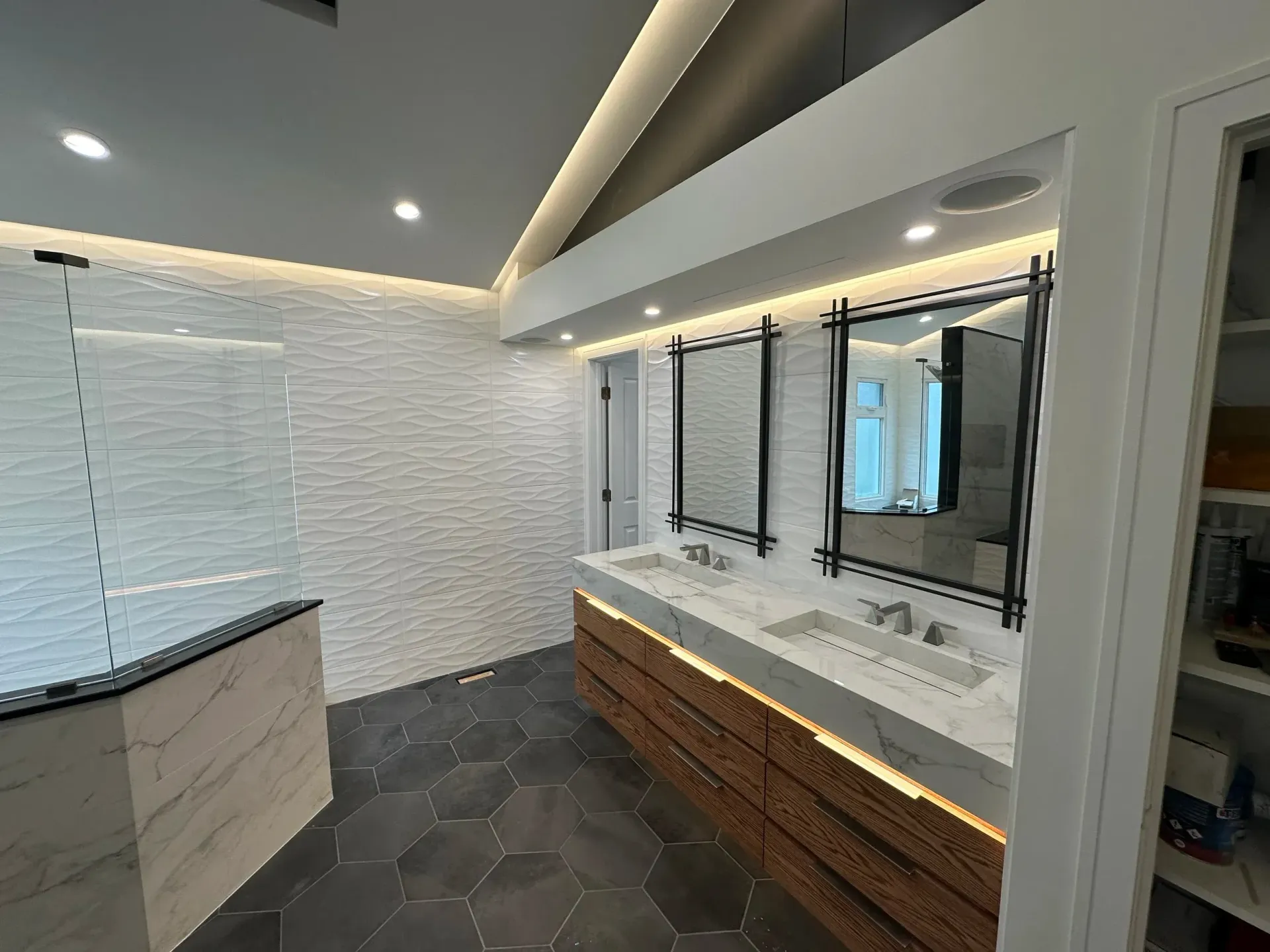 Modern bathroom with long vanity, large mirror, dark floor tiles, and white brick walls under recessed lighting