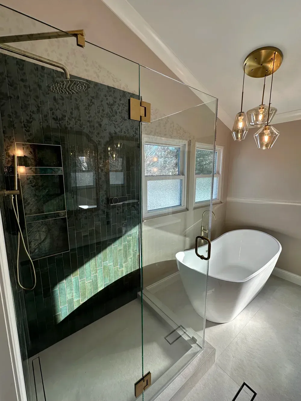 Modern bathroom with glass shower, white freestanding tub, black tile wall, and brass chandelier