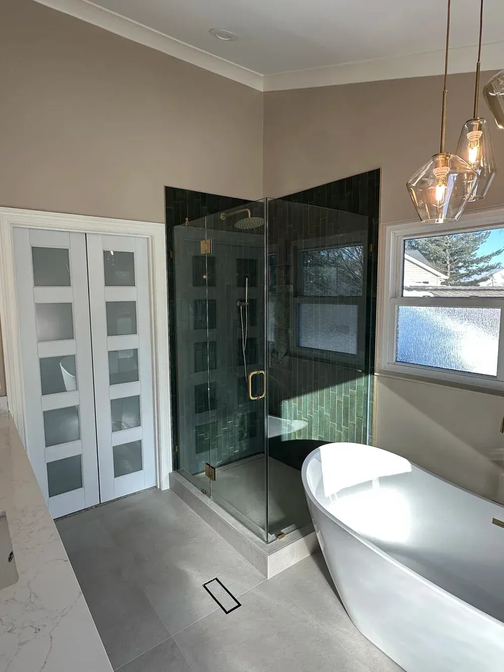 Modern bathroom with glass shower, white double doors, and freestanding tub by a window.