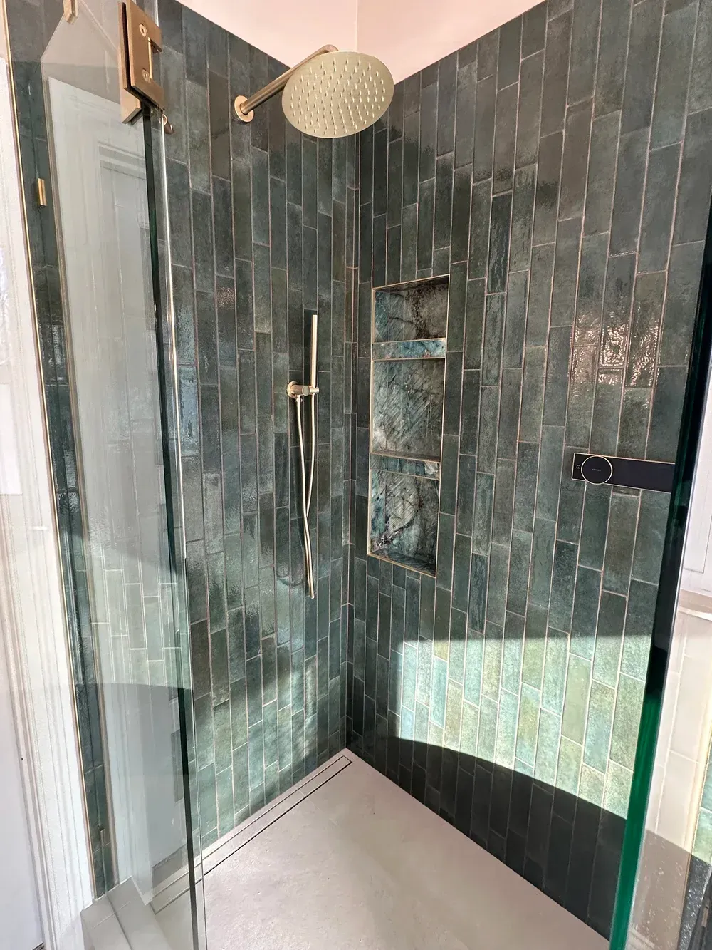 Walk-in shower with dark tile walls, glass door, and large round rainfall showerhead