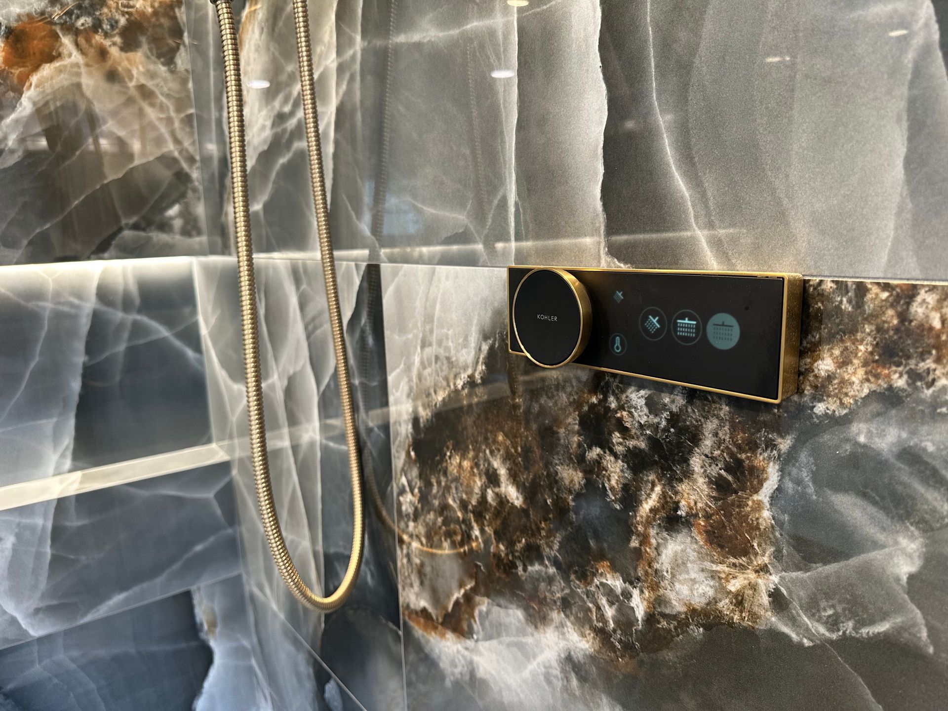 Gold chain hanging beside a black smartwatch on a gray marble wall panel