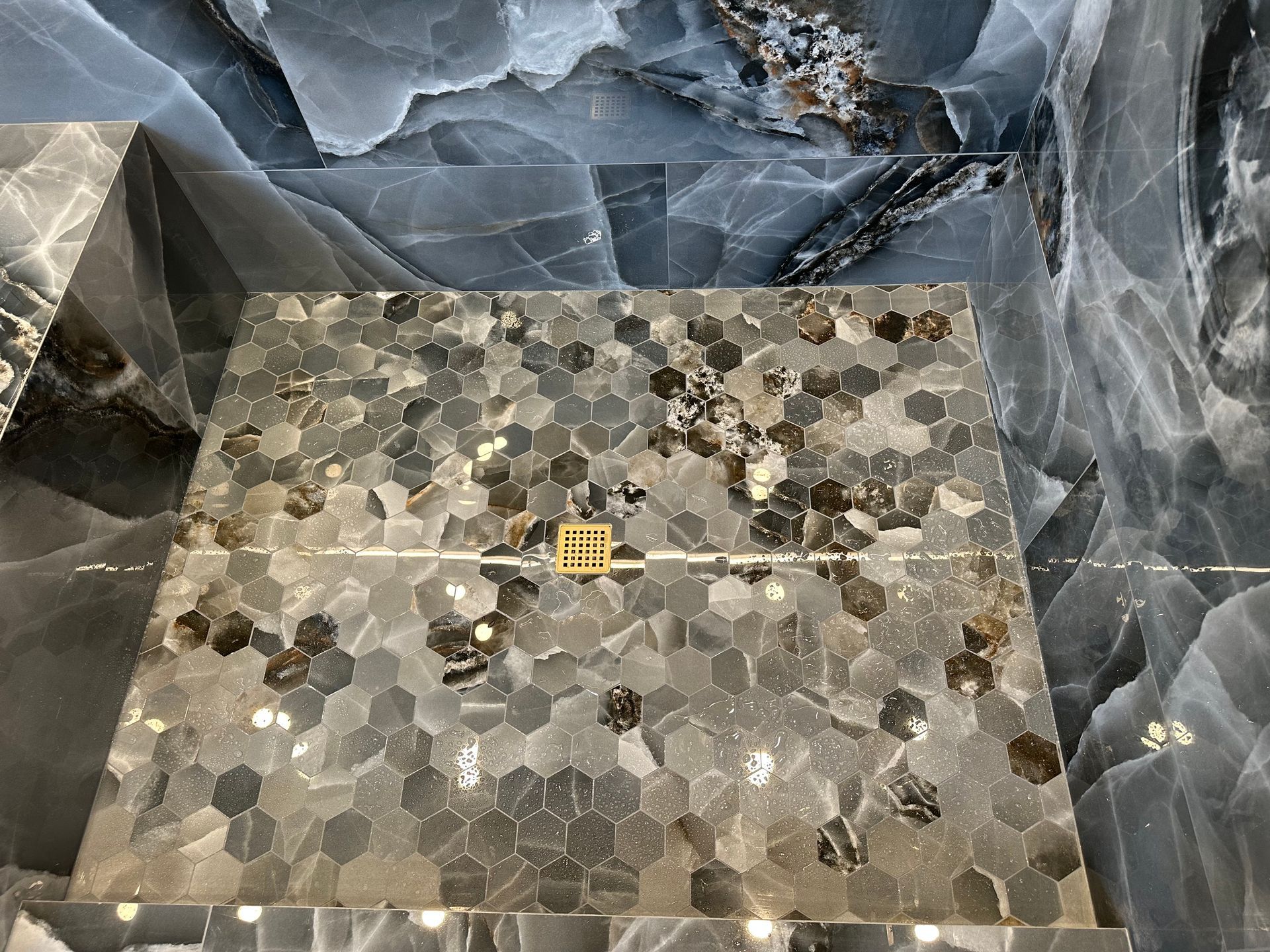 Stone shower floor with hex tile and a small yellow drain cover, surrounded by gray marble walls
